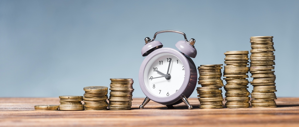 Sie sehen eine Uhr und stetig steigende Stapel von Geldmünzen